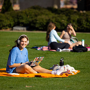 A student smiles for the camera while working on a laptop and laying on a UT blanket at the Humanities Plaza-North lawn on March 23, 2023. Photo by Steven Bridges/Steven Bridges/University of Tennessee. 