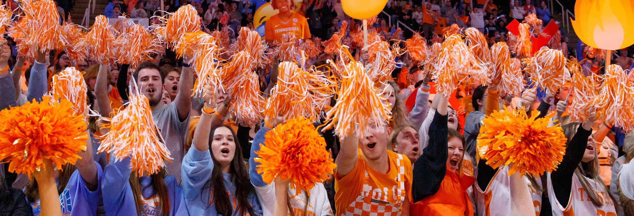 The student section at the UT Lady Vols basketball game shake their orange and white pom poms to the camera up close.