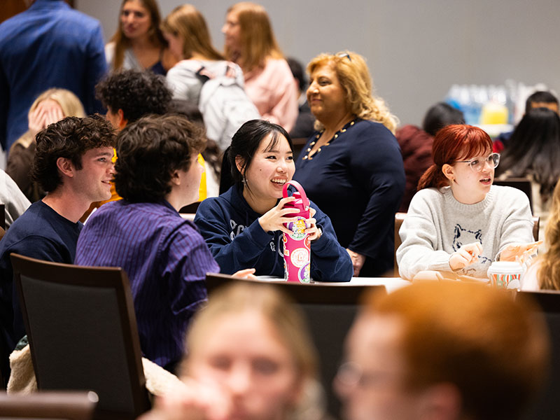 Groups of students sit around circular tables, laughing and conversing during a Friendsgiving event.