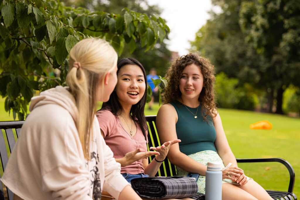 A group of three individuals sitting on a bench outside talking