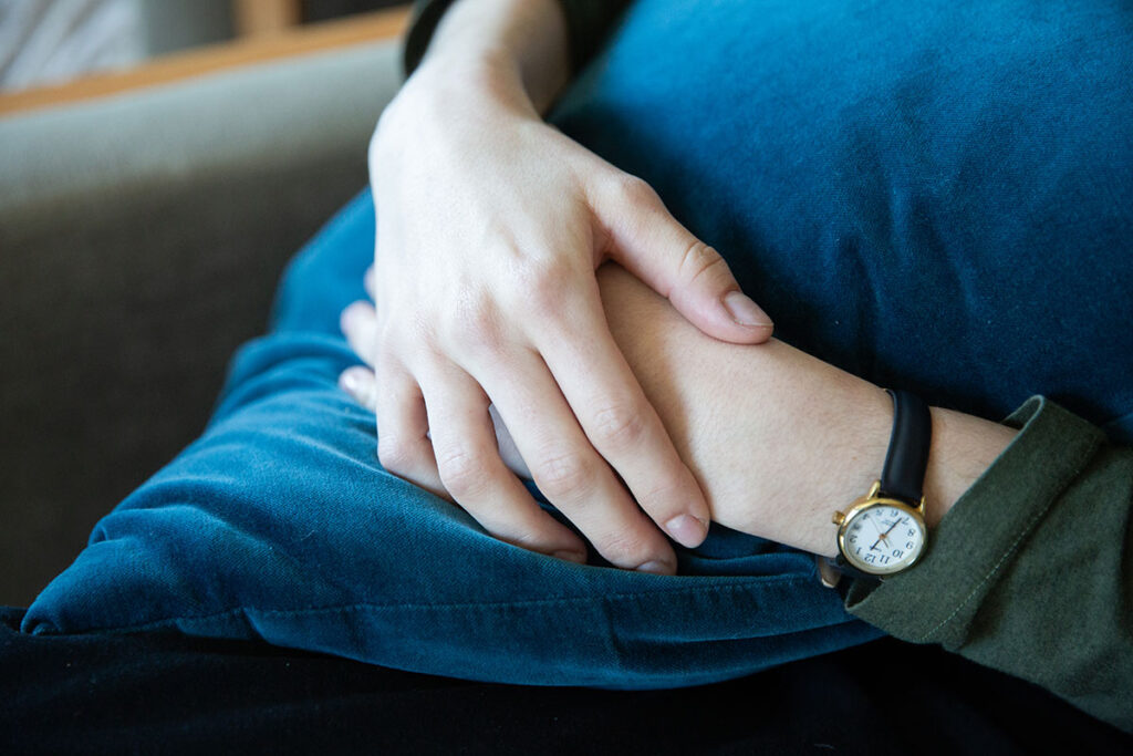A student's hands hugging onto a blue pillow during a therapy session. They have a analog watch on their left hand and their right hand is on top of their left.