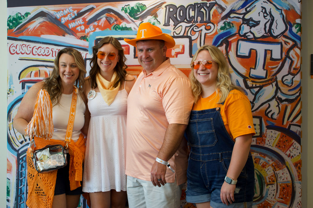 A family at Fall Family Weekend is smiling for a picture in front of a University of Tennessee-themed backdrop.