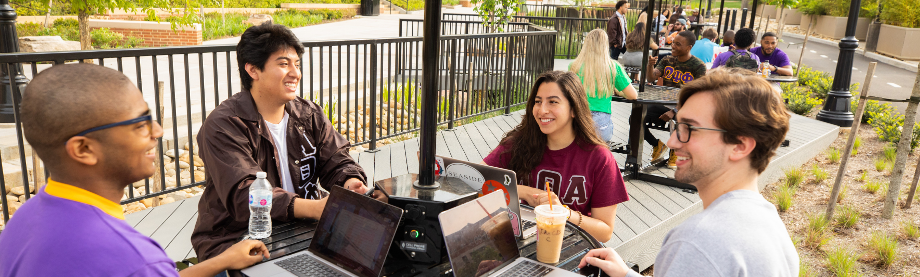 Various members of the Multicultural Greek Council gathered around a table outside of Brown Hall. This photo represents the Cross Council Exchange.