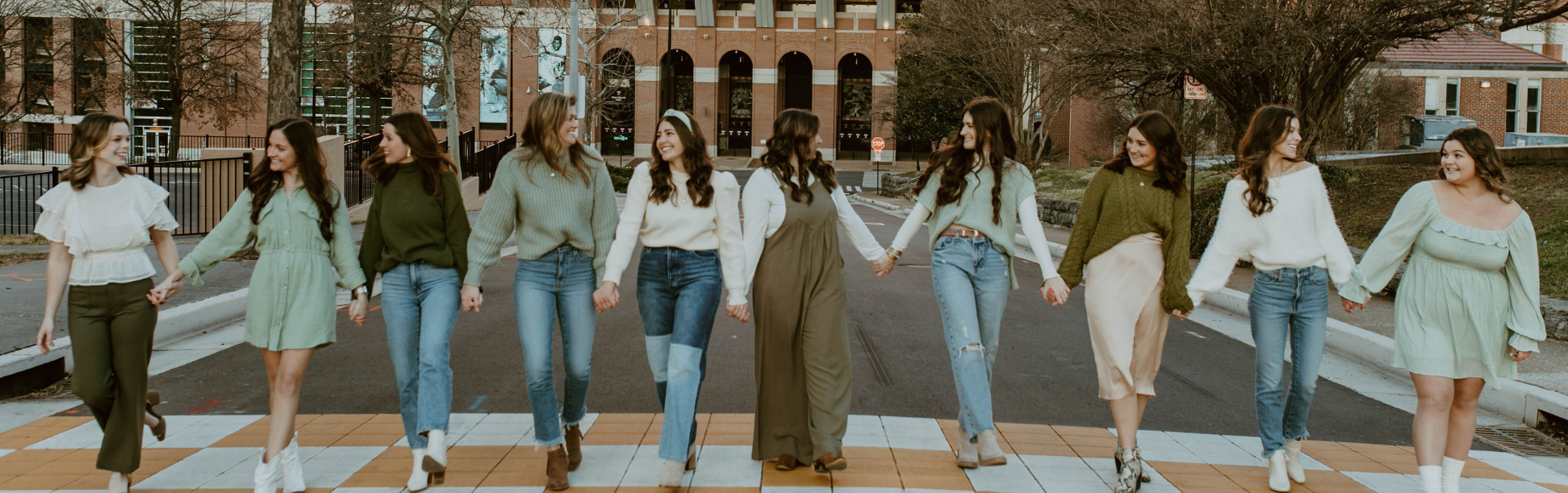 Members of the Panhellenic Council Executive Board holding hands and smiling at each other. They are walking away from Neyland Stadium across the orange and white checkerboard crosswalk.