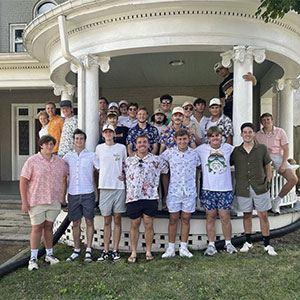 Local members of Delta Chi are posing in front of a fort house. They are all in Hawaiian shirts.