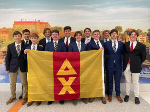 Members of Delta Chi holding their fraternity flag, which is red and yellow. They are all dressed in suits in front of a wall of the student union at the University of Tennessee, Knoxville.