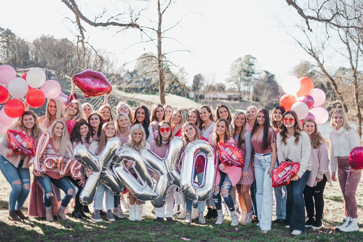 Several members of Delta Zeta smiling for a Valentine's Day photoshoot. They are all outside and wearing pink, red, and white outfits.