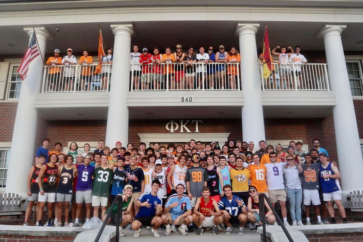 Dozens of members of Phi Kappa Tau at the University of Tennessee, Knoxville smiling in front of their fraternity house. They are all wearing sports jerseys.