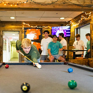 One fraternity member of Sigma Chi playing pool within his fraternity house during the IFC recruitment. Members of Sigma Chi are looking on in the background.