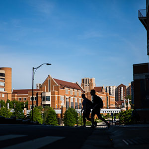 Two silhouette students are walking across Peyton Manning pass. The pedestrian bridge and the student union can be seen in the background.