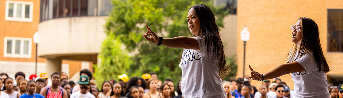 A member of the Multicultural Greek Council on Stage during Meet the Greeks outside of the Student Union. She is holding up her sorority's hand symbol.