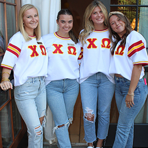 Four members of Chi Omega smiling for a group photo in their red, yellow, and white bid day jerseys.