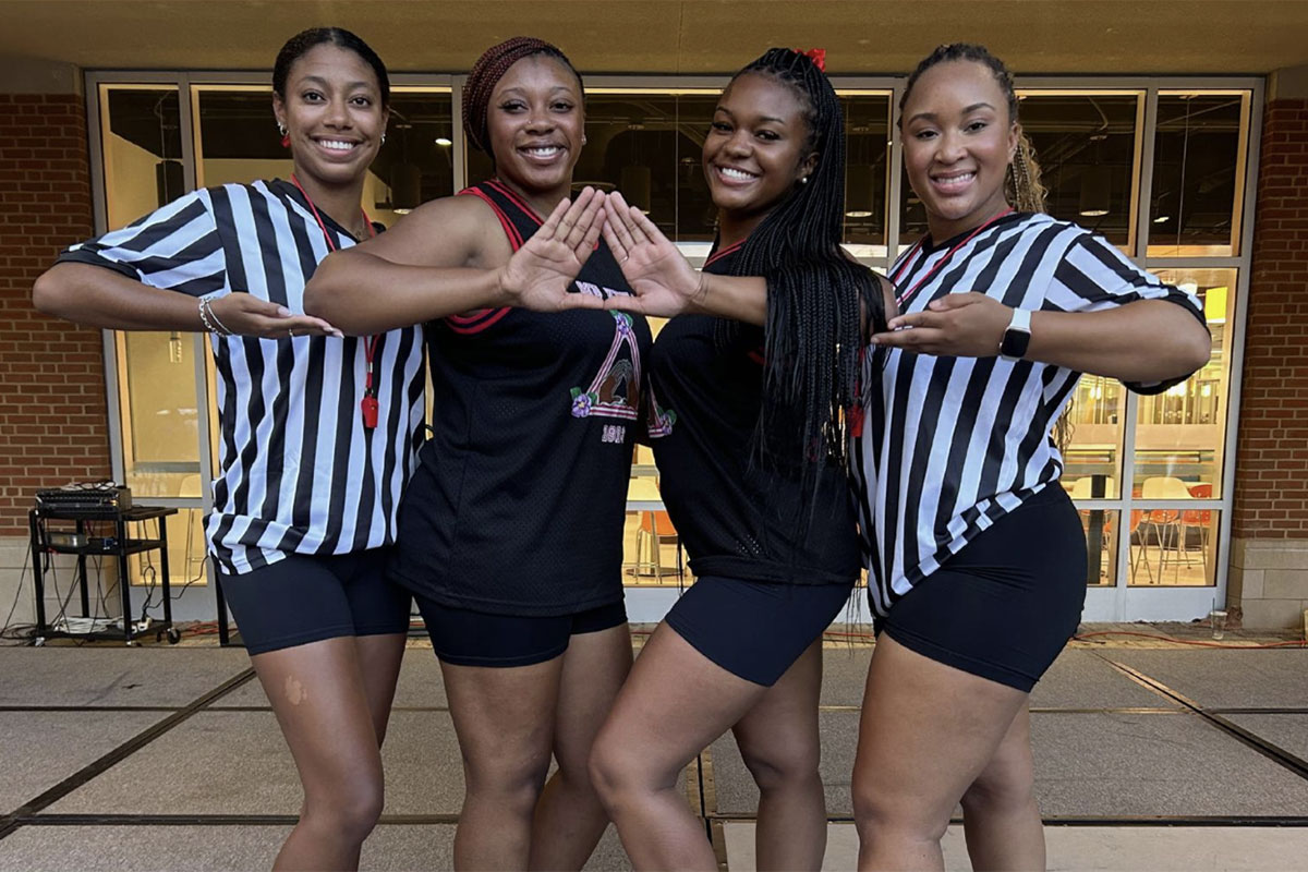 Four members of Delta Sigma Theta Sorority, Inc. posing for a photo outside of the Student Union. They are on stage for a step event.