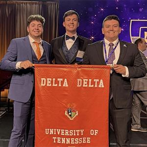 Local members of Delta Tau Delta holding up an orange "Delta Delta" chapter flag at a national conference.