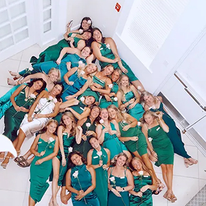 Members of Delta Zeta laying in the front room of their sorority house. They are all wearing cream and green dresses and holding white roses.