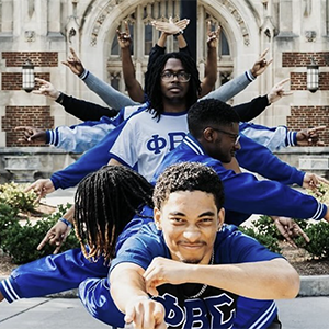 Members of Phi Beta Sigma Fraternity, Inc. outside of Ayers Hall. They are arranged in a formation while holding up hand symbols.