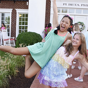 Two local members of Pi Beta Phi outside of their sorority house in Sorority Village smiling during work week.
