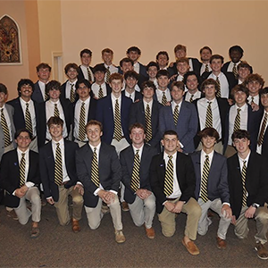 Newly initiated members of Sigma Nu smiling for a group picture. They are all in wearing suits with a gold and black tie.