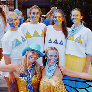 Six members of Delta Delta Delta at the University of Tennessee, Knoxville during work week. They are all wearing yellow, blue, and white. They are standing outside of their sorority house in Sorority Village.