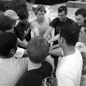 Members of the fraternity, Beta Theta Pi. are gathered. Each person has a hand in. The picture is in black and white. This is representing the national website.