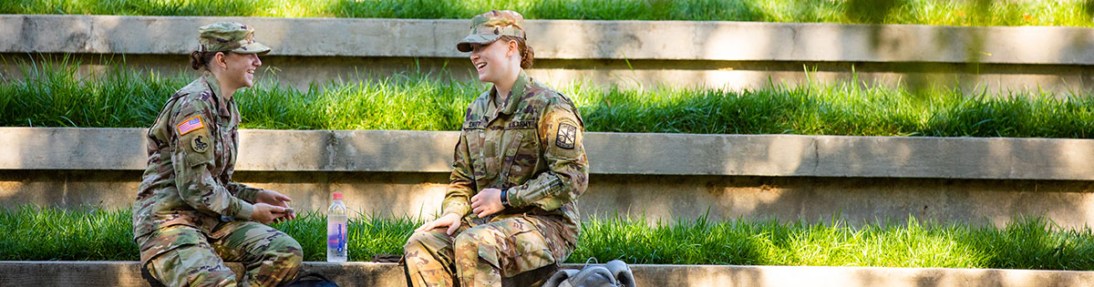 Two military students sitting in the amphitheatre on campus, smiling and talking to each other.