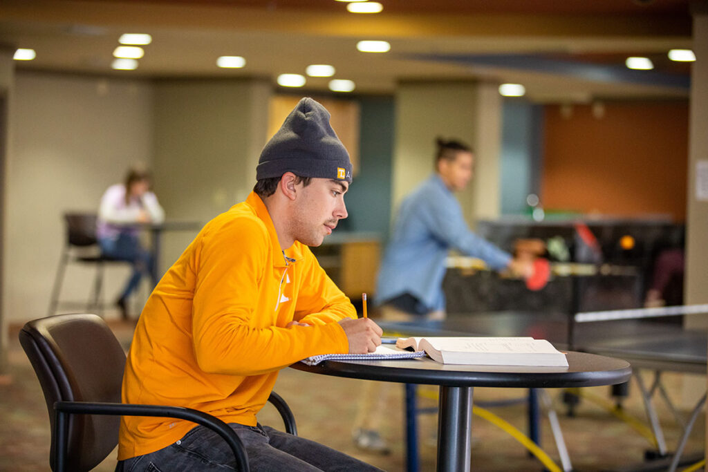 A student wearing an orange shirt, gray Tennessee beanie studying in Volunteer Hall