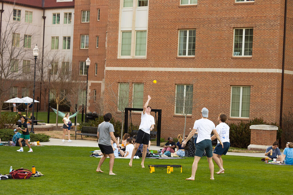 Four play spikeball in the courtyard on a sunny day.