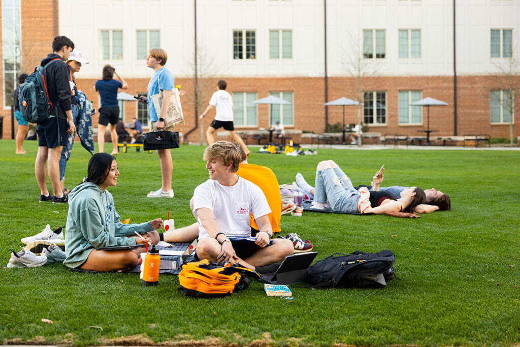 Students relaxing in the courtyard either studying or looking at their cellphones during a warm February day.