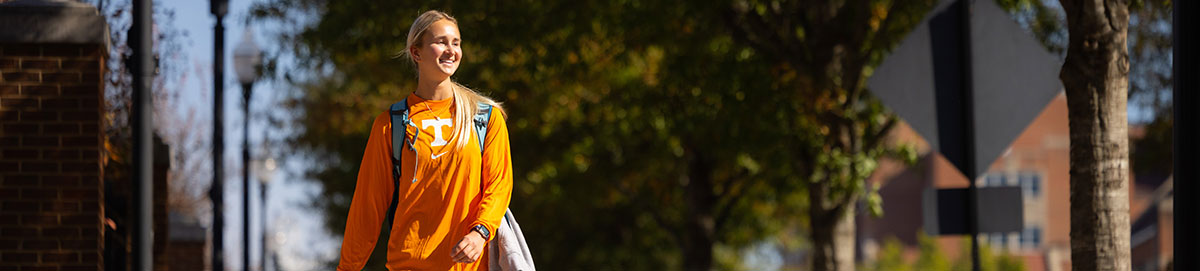 A student smiling wearing an orange UT longsleeve shirt while she walks on campus