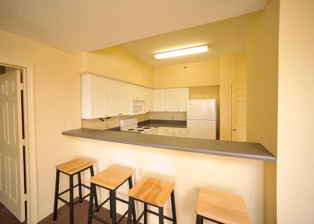 Four barstools overlooking the kitchen with white cabinets and white appliances