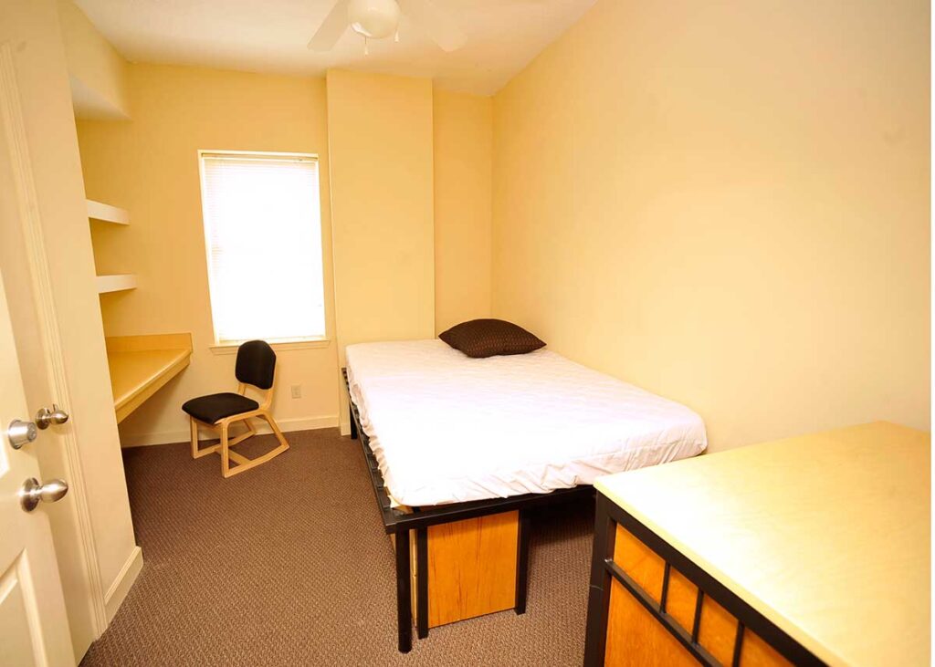 An undecorated bedroom that is slightly lofted with storage underneath and a built in desk with a chair