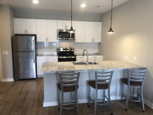 The kitchen island with three barstools, two pendant lamps, white cabinets and stainless steel appliances