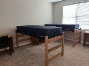 An undecorated shared bedroom that has two lofted bed and two desks