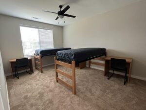 An undecorated shared bedroom that has two lofted bed and two desks