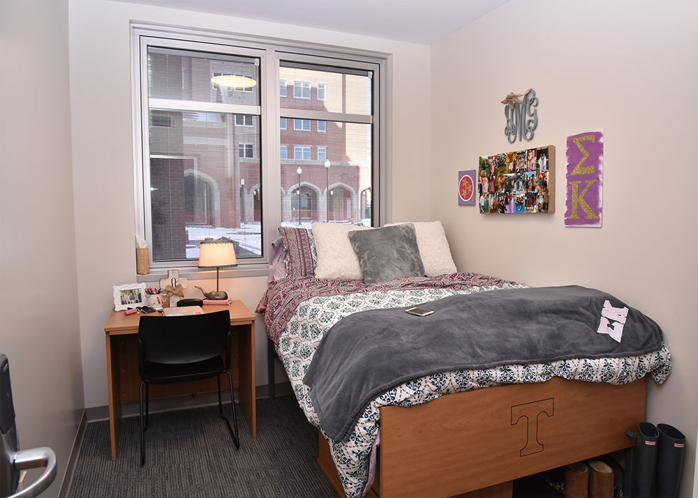 A bedroom that has the bed on the right and a small desk on the left. The walls are decorated with Sigma Kappa decor