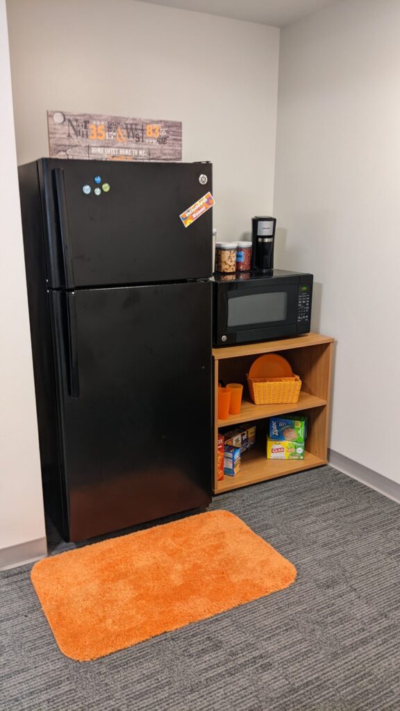 A nook for a full sized fridge and a small cabinet to the right to hold food with a microwave on top