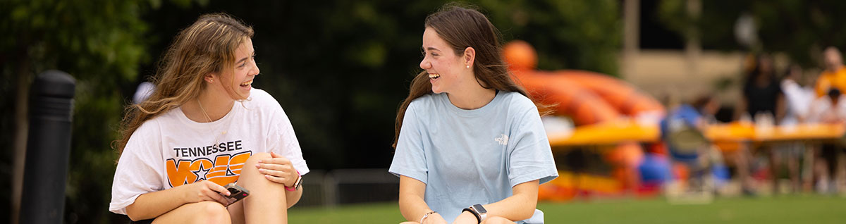 Two female students smiling at each other while sitting outside