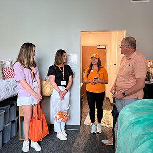 A housing tour guide is showing a mother, father and their daughter around the dorm rooms on campus