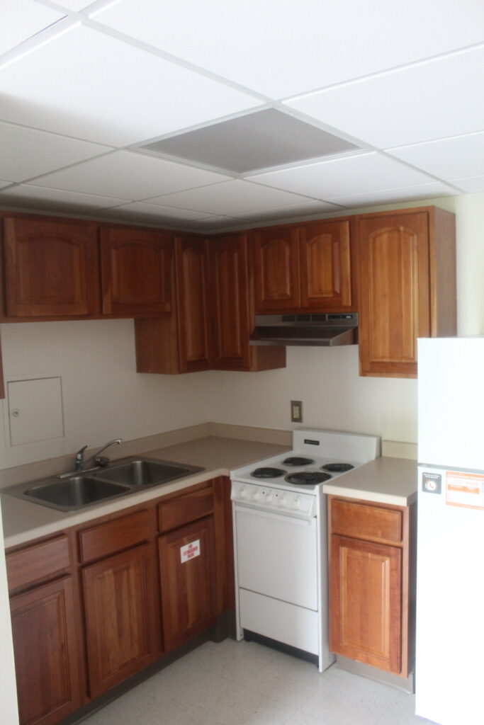 An L-shaped kitchen with a white four-burner stove, double sink and brown cabinets