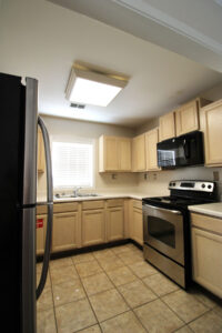 A view of the kitchen featured light toned wood cabinets, a double stainless steel sink, a window above the sink and a stainless steel fridge and dishwasher