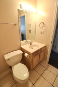 A photo of a single sink vanity with a vertical mirror above it and the toilet situated to the left