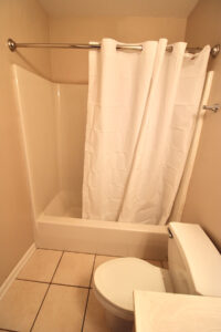 The toilet and a bathtub/shower combo that has a white shower curtain hanging on the rod