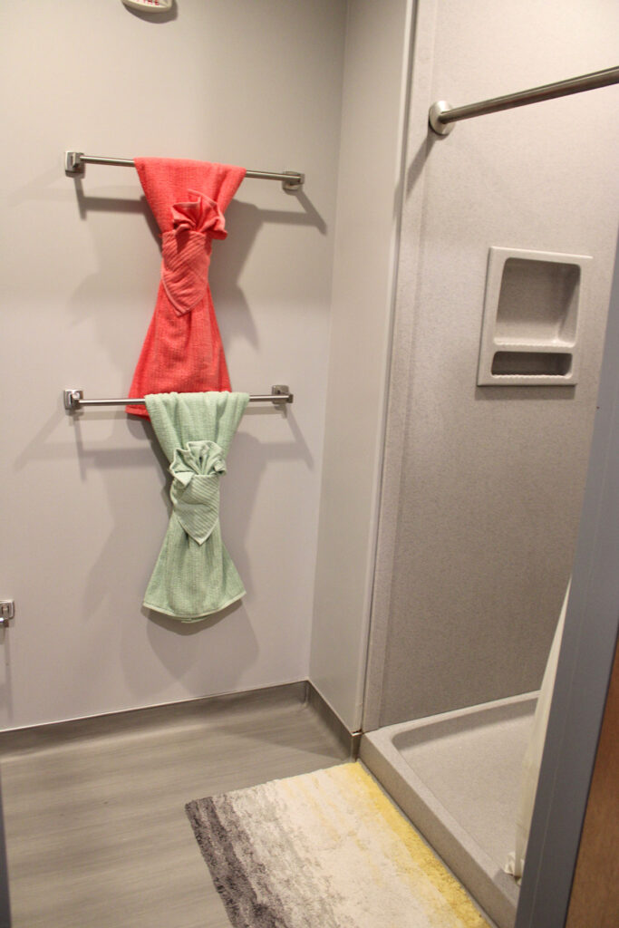 Two towels hanging on two towel racks outside of a walk in shower