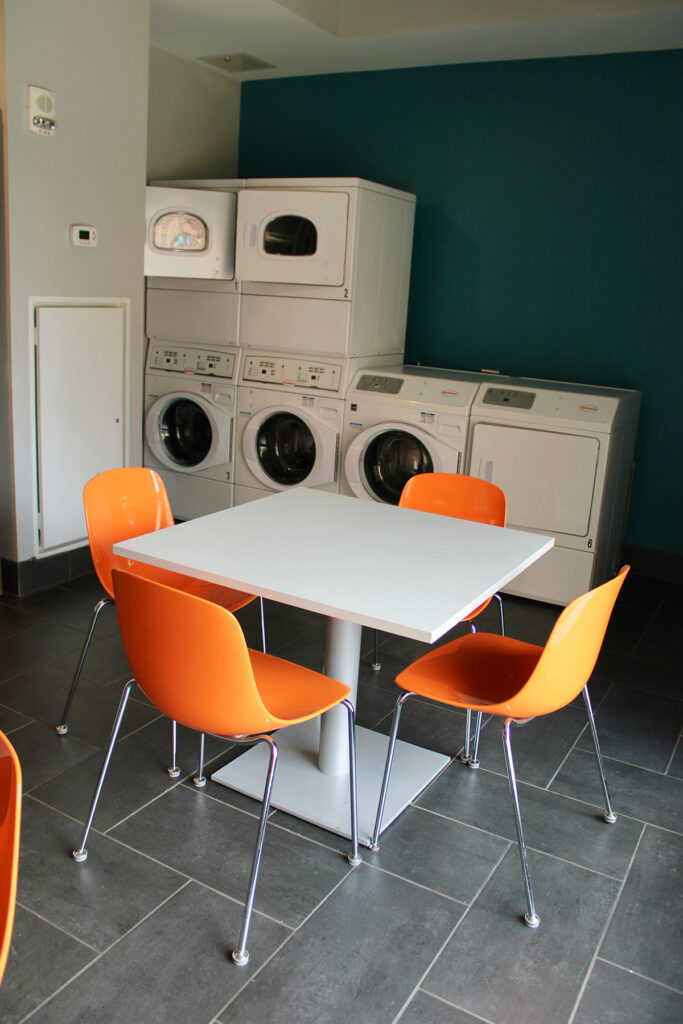 The laundry room in Magnolia Hall that has a table with four orange chairs surrounding it