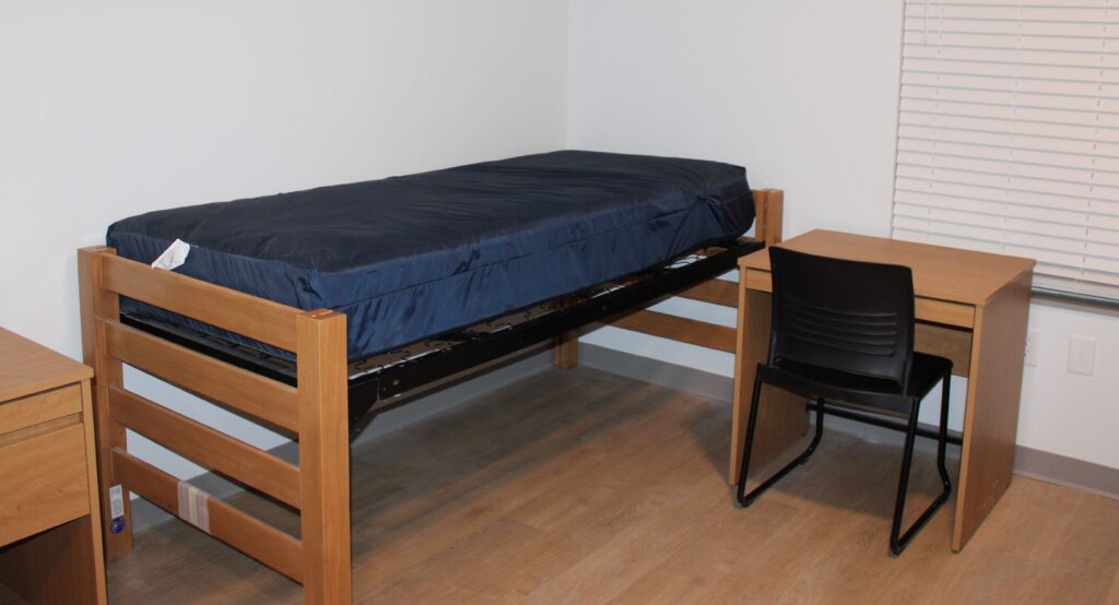 A single bed with a small desk and chair beside it