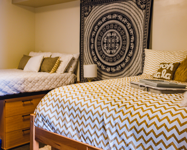 A decorated bedroom in Brown Hall that has lofted beds and has storage underneath it and a tapestry hanging between the two beds
