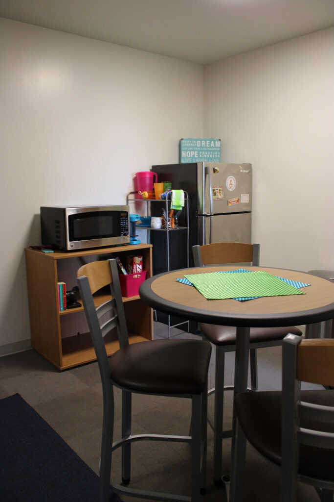 A living area that has a round table with elevated chairs, a stainless steel fridge and a microwave