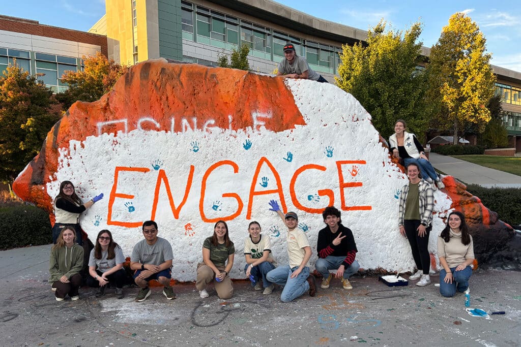 Students involved in Engage LLC 2025 paint the rock with the words "Engage".