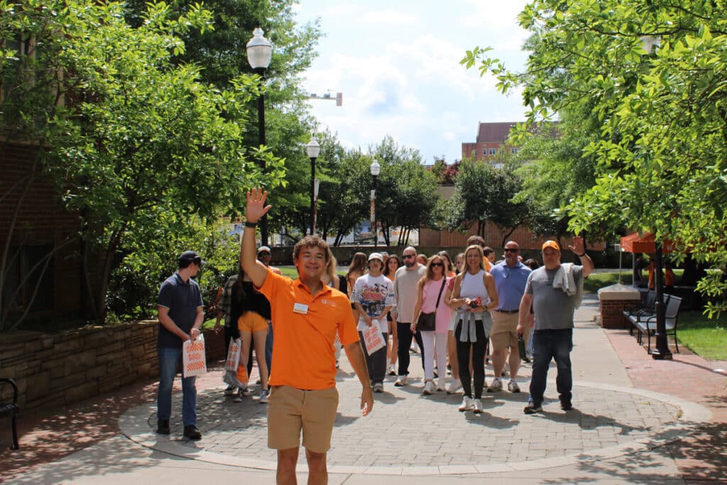 a student waving in front of a large group of people mingling