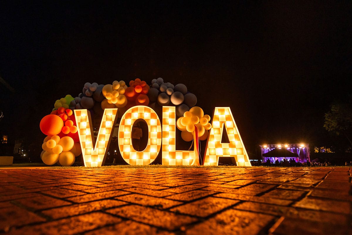 A checker boarded Vola sign decorated with lights and balloons during 20th Anniversary of Volapalooza in Circle Park.